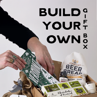 Person building a gift box with various Vermont-themed products on a white background.
